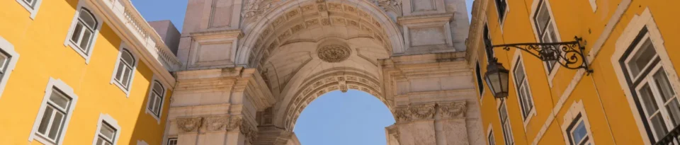 Low-angle view of the Rua Augusta Arch in Lisbon, Portugal, framed by vibrant yellow buildings under a clear blue sky.